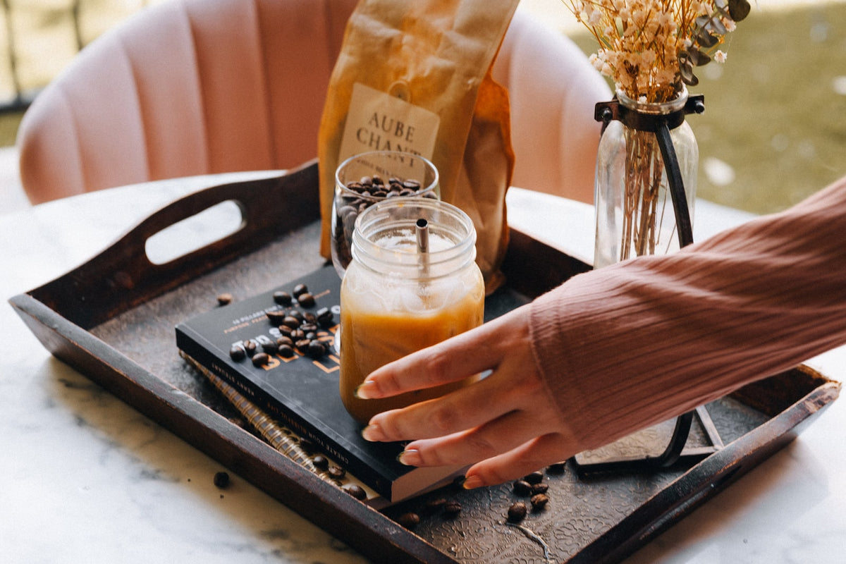Aube Chant coffee bag and iced coffee on a tray beside flowers