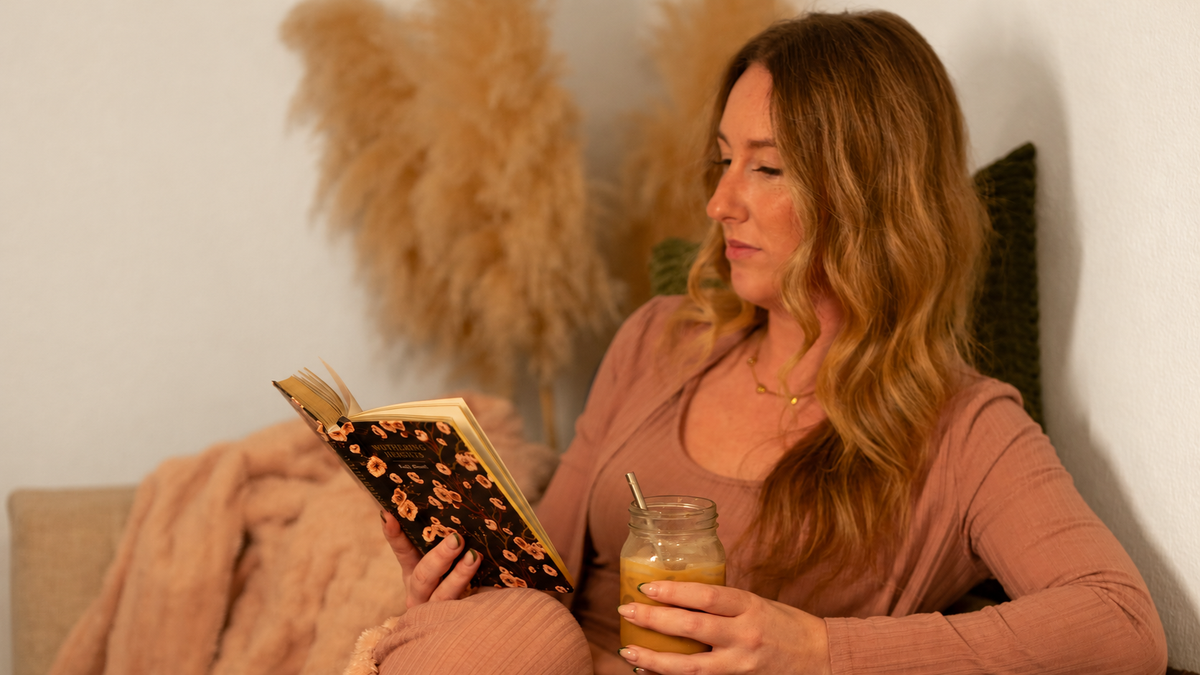 Caitie reading a book with an iced coffee during a quiet morning